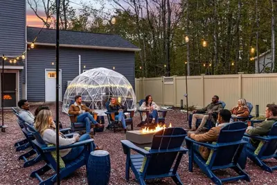 a group of people sitting in chairs around a fire pit at The Poconest - Luxurious Mountain Mansion in Long Pond