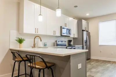 a kitchen with white cabinets and a sink and two bar stools at 4Bedrm,4Bath-BackyardWiFi WDCoffeeParking in Philadelphia