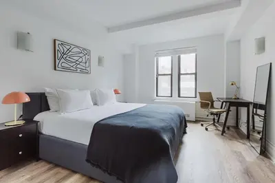 a white bedroom with a bed and a desk and a table at Blueground Upper West Side fitness center nr Central Park NYC-1596 in New York