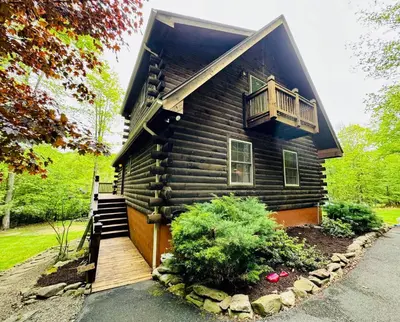 a wooden house with a porch and a balcony at Lazy River Cabin: Lakefront Stay in Greentown