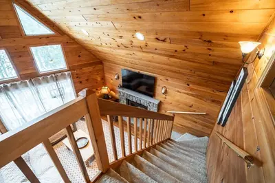 a staircase in a log cabin with a fireplace at Lazy River Cabin: Lakefront Stay in Greentown