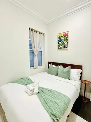a white bedroom with two beds and a window at Travelers Dream that's Mins to NYC having Game Room and Parking in Jersey City