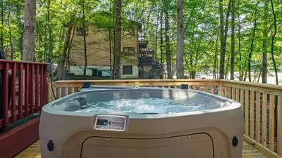 a hot tub on a deck with trees in the background at Pirate-Themed Lakefront Home w Kayaks Game Room Views Hidden Treasure Hunt in East Stroudsburg