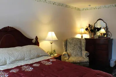 a bedroom with a bed and a chair and a mirror at The White Birch Inn in Berwick