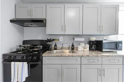 a kitchen with white cabinets and a stove and a sink at Peaceful Hideaway - NYC & NWK with free parking in Newark