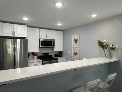 a kitchen with white cabinets and a stainless steel refrigerator at 15% OFF | EWR| NYC | Metropolis Serenity Haven in Newark
