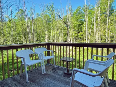 three chairs and a table on a deck with trees at Designer Poconos Chalet I Ski, Skate, Lakes, Family-Friendly in Lake Ariel