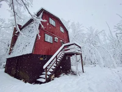 a red cabin in the snow with a staircase at Designer Poconos Chalet I Ski, Skate, Lakes, Family-Friendly in Lake Ariel