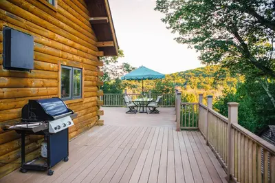 a grill on a wooden deck next to a house at Rustic Ridge Log Cabin: Hot Tub, Games, Views! in Mount Pocono