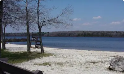 a bench on a beach next to a body of water at Lakeside Escape at StillwaterHot Tub & Ski in Pocono Summit