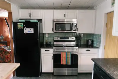a kitchen with a black refrigerator and white cabinets at Mountain Laurel Bungalow Lakeview & Ski in Lake Harmony