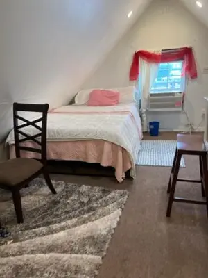 a bedroom with a bed and a chair and a window at Atic Apartment in Perth Amboy