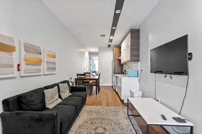 a living room with a black couch and a kitchen at 2 Queen Beds, TV's in Bedroom, Path to Manhattan in Jersey City