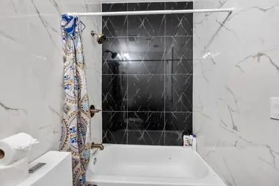 a bathroom with a white tub and a black tile wall at 2 Queen Beds, TV's in Bedroom, Path to Manhattan in Jersey City