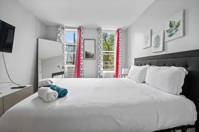 a white bedroom with a large white bed and a window at 2 Queen Beds, TV's in Bedroom, Path to Manhattan in Jersey City