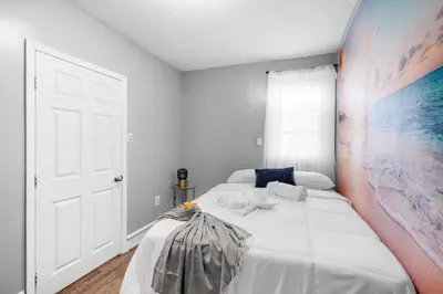 a bedroom with a white bed with a painting on the wall at Bright Corner Flat near Transit and Trails in Philadelphia