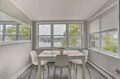a dining room with a table and chairs and windows at Cozy Lakefront House with a private dock and lake in Hopatcong