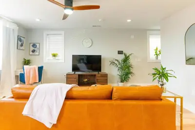 a living room with a orange couch and a flat screen tv at Elegant Urban Escape - 2 Bedrooms, 1 king Bed and 1 Queen Bed, Gated Private Entrance and Parking in Philadelphia