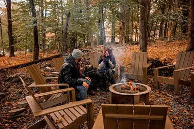 two people and a dog sitting around a fire at Luxurious Cabin by Lakes & Ski in Lake Ariel