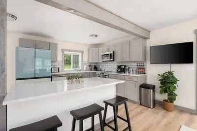 a white kitchen with a large white counter and stools at Nature Getaway - Creek, Firepit, Deck, Privacy - Delaware River in Sparrow Bush