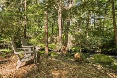a white chair sitting in the woods next to a creek at Nature Getaway - Creek, Firepit, Deck, Privacy - Delaware River in Sparrow Bush
