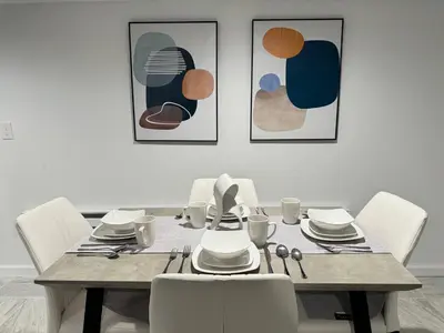 a dining room table with white chairs and paintings at Open Serene Suite - 10mins-EWR, 25mins-NYC in Irvington
