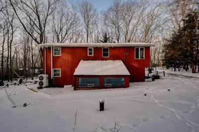 a red house with snow on it in the snow at Cozy mountain house with beach access and firepit in Lake Harmony