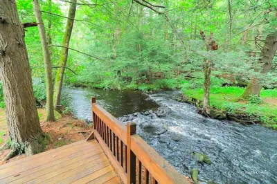 a wooden bridge over a river in a forest at Traditional Wooden Cabin Rental in the Poconos, Pennsylvania in Canadensis