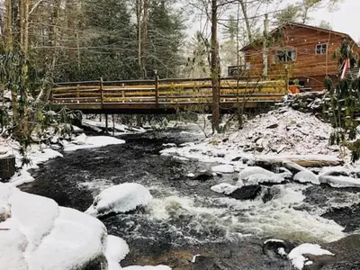 a bridge over a stream with snow on the ground at Idyllic Log Cabin Rental with a Porch in the Poconos of Pennsylvania in Canadensis