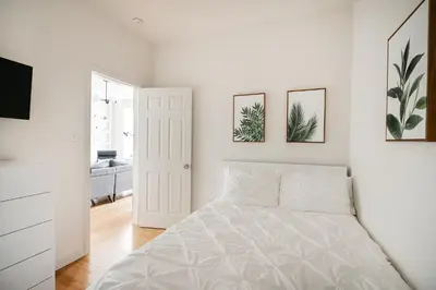 a white bedroom with a bed and two pictures on the wall at Beautiful 3 Bedroom Unit in Prime Location in New York