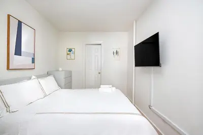 a white bedroom with a bed and a flat screen tv at Prime Upper west Side Location 1 Bedroom Apt in New York
