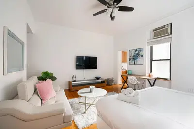 a white living room with a couch and a tv at Bright and Comfy Studio in NYC in New York