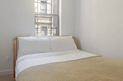 a bedroom with a bed with white sheets and a window at Blueground Chinatown washer nr City Hall NYC-1871 in New York