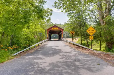 a covered bridge on a road with trees at Honey Bee Farm On-Site Susquehanna Valley Apt! in Dalmatia