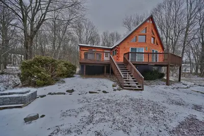 a wooden house with a deck in the snow at NEW ! Lake front Lookout Log Cabin! Private Lake ! in White Haven