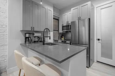 a kitchen with white cabinets and a stainless steel refrigerator at Modern Nolita Hideaway in New York