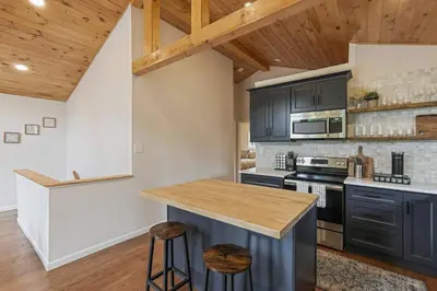 a kitchen with black cabinets and a wooden ceiling at Pocono Chalet with Sauna/Hot Tub/Firepit/10+ Beds in Long Pond