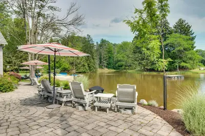 a patio with chairs and an umbrella next to a lake at Fish and Hike Lakeside Poconos Retreat, Unit 3 in Bangor