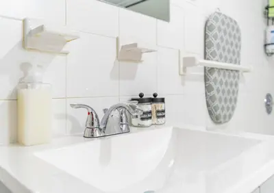 a white bathroom with a sink and a mirror at Cozy Private Room in Shared Space NYC Light Rail in Bayonne