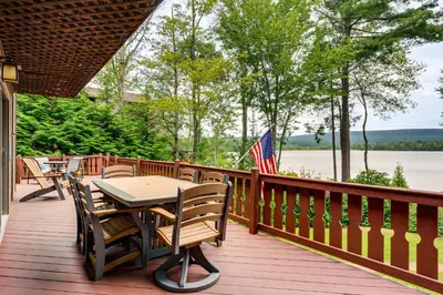 a wooden deck with tables and chairs and an american flag at Beech Mt Lakefront Gem! Hot Tub, Kayaks, Billiards