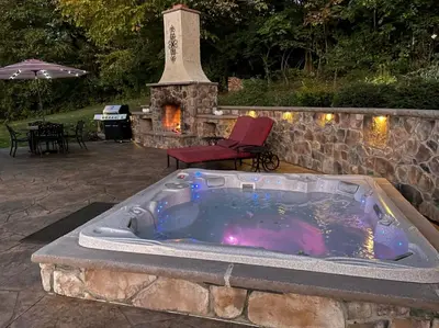 a hot tub in front of a stone wall with a fireplace at Fantastic A-Frame Cabin for a Couples' Getaway near Robesonia, Pennsylvania in Robesonia
