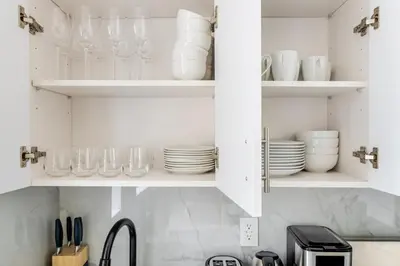 a kitchen with white cabinets with plates and glasses at Blueground Midtown West washerdryer nr Central Park NYC-1876 in New York