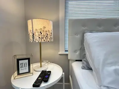 a bed with a table with a lamp and two remote controls at New 1BR Walk to Pats & Genos in Philadelphia