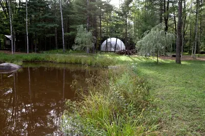 a greenhouse in a field next to a body of water at Incredible Spacious Dome for A Group Glamping Experience Surrounded by Nature in Woodridge, New York in Woodridge