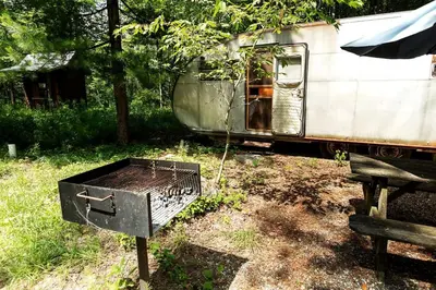 an old trailer with a grill in front of it at Gorgeous Fully Restored Caravan Nestled in the Trees Along Silver Lake for a Unique Vacation in Woodridge, New York in Woodridge