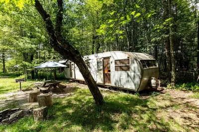 a trailer parked in the woods with a picnic table at Gorgeous Fully Restored Caravan Nestled in the Trees Along Silver Lake for a Unique Vacation in Woodridge, New York in Woodridge