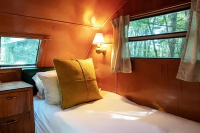 a bedroom with a bed and two windows at Gorgeous Fully Restored Caravan Nestled in the Trees Along Silver Lake for a Unique Vacation in Woodridge, New York in Woodridge