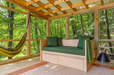 a screened in porch with a hammock in the forest at Sunlit Airstream in Trees with Expansive Deck Nature Views in De Lancey