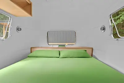 a bed in a small room with two windows at Sunlit Airstream in Trees with Expansive Deck Nature Views in De Lancey
