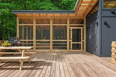 a screened in porch of a house with a picnic table at Sunlit Airstream in Trees with Expansive Deck Nature Views in De Lancey